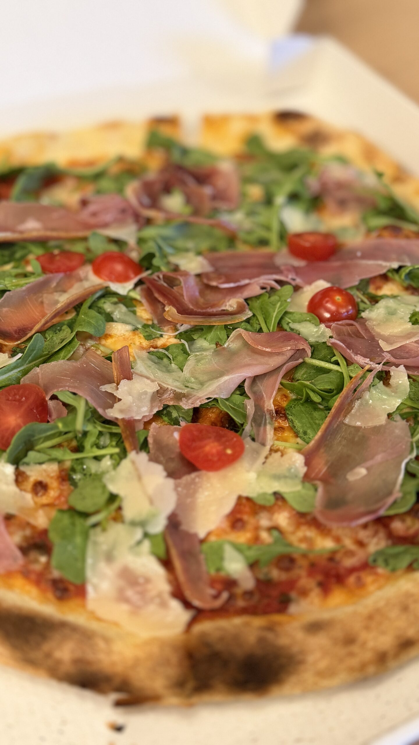 Pizza garnie de jambon cru, roquette, copeaux de parmesan et tomates cerises, sur son carton, à La Rosière