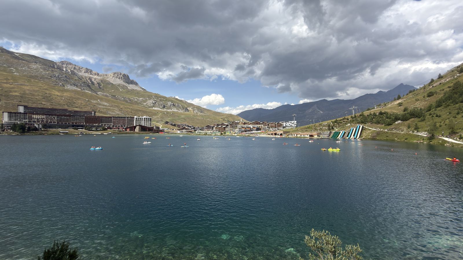 Le lac de Tignes sous un ciel chargé, eau turquoise transparente au premier plan
